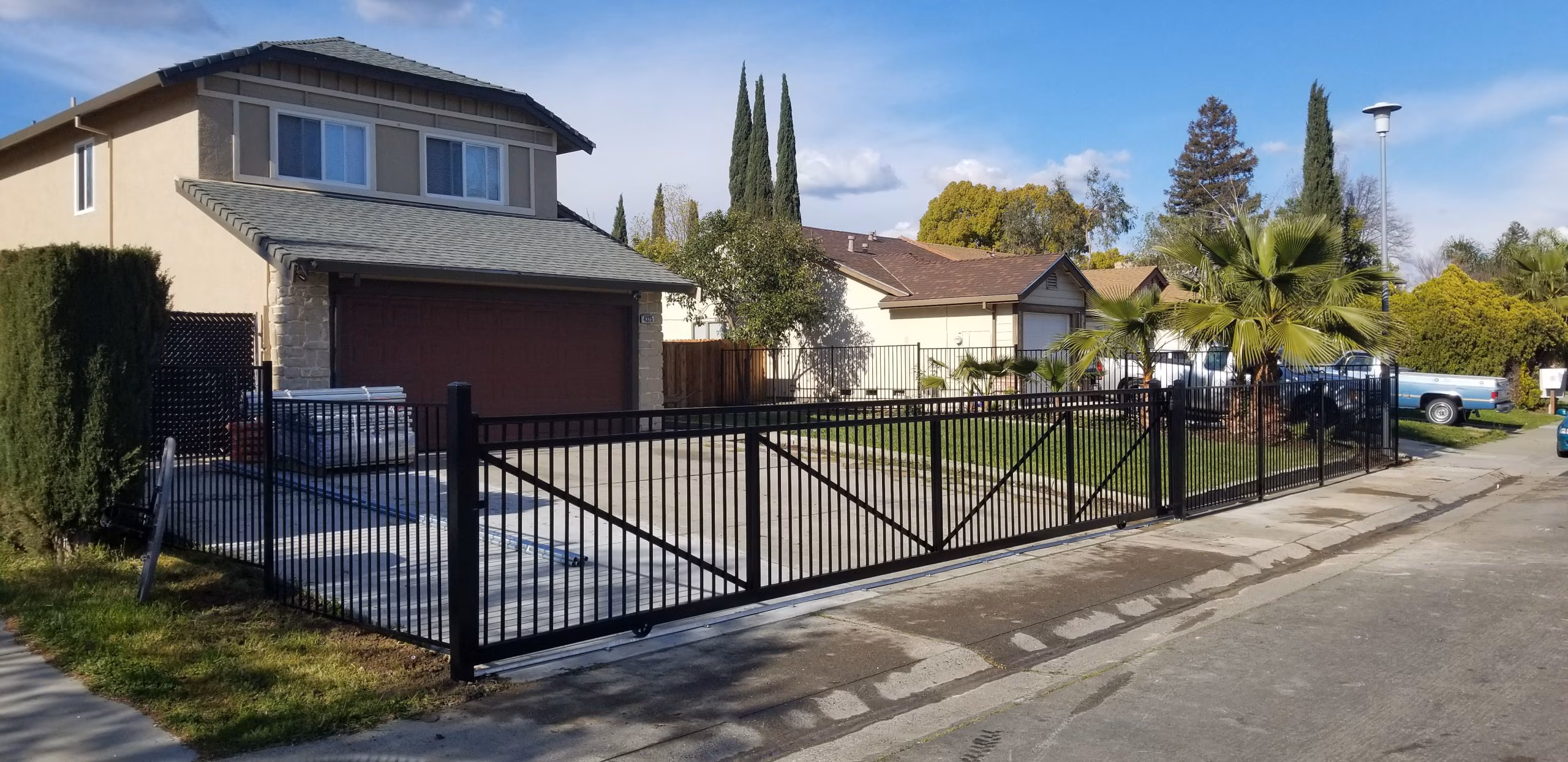 Black ornamental metal fence with a large double driveway gate installed along the front of a residential property.